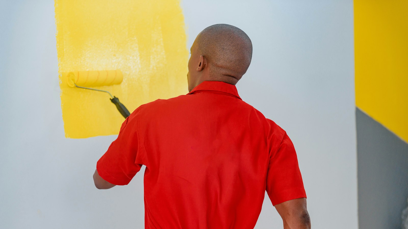 A man painting a wall with yellow paint
