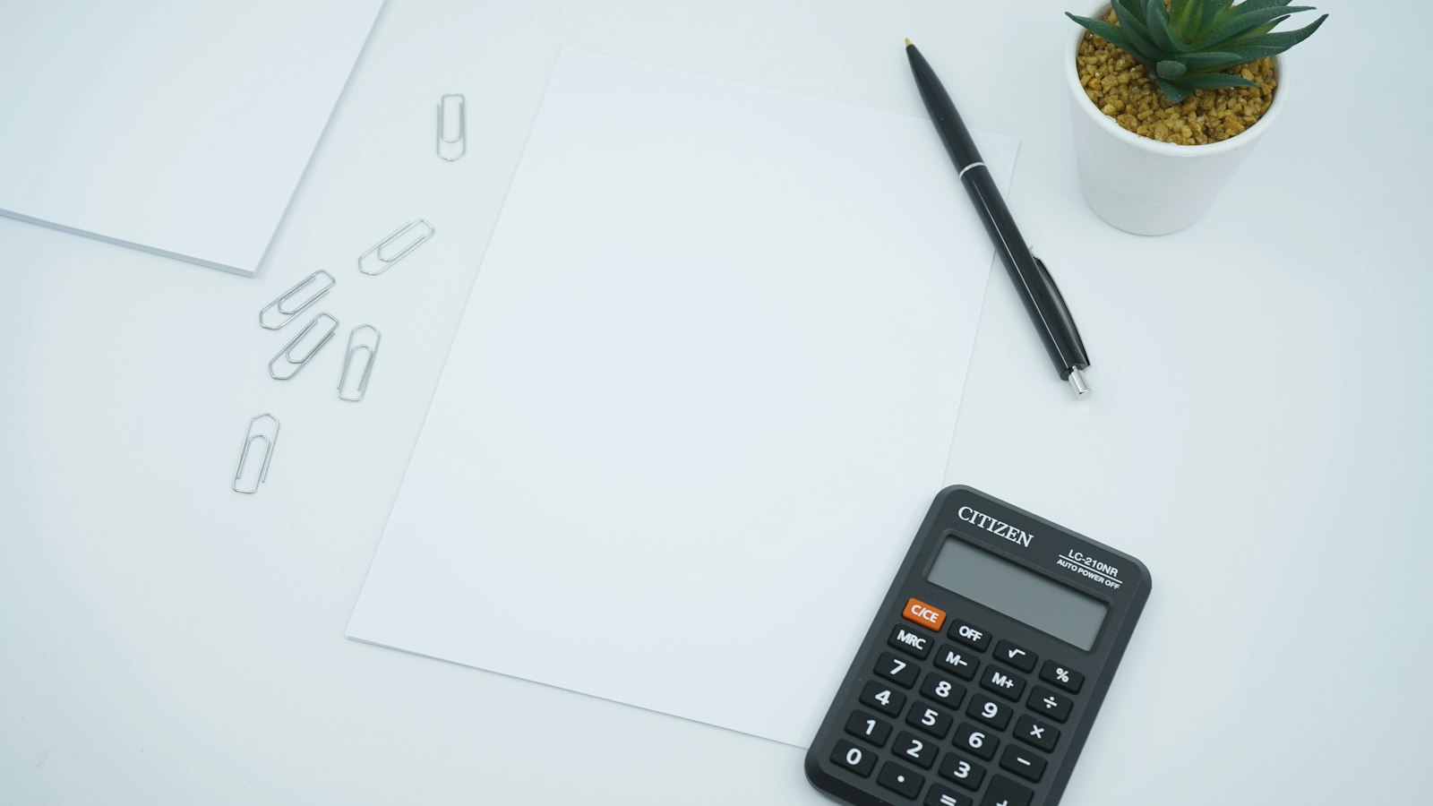 Black calculator beside black pen on white printer paper