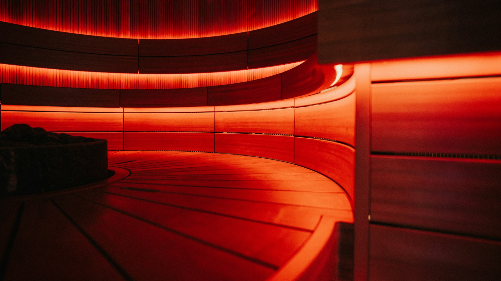 Curved wooden sauna benches illuminated by warm red ambient lighting